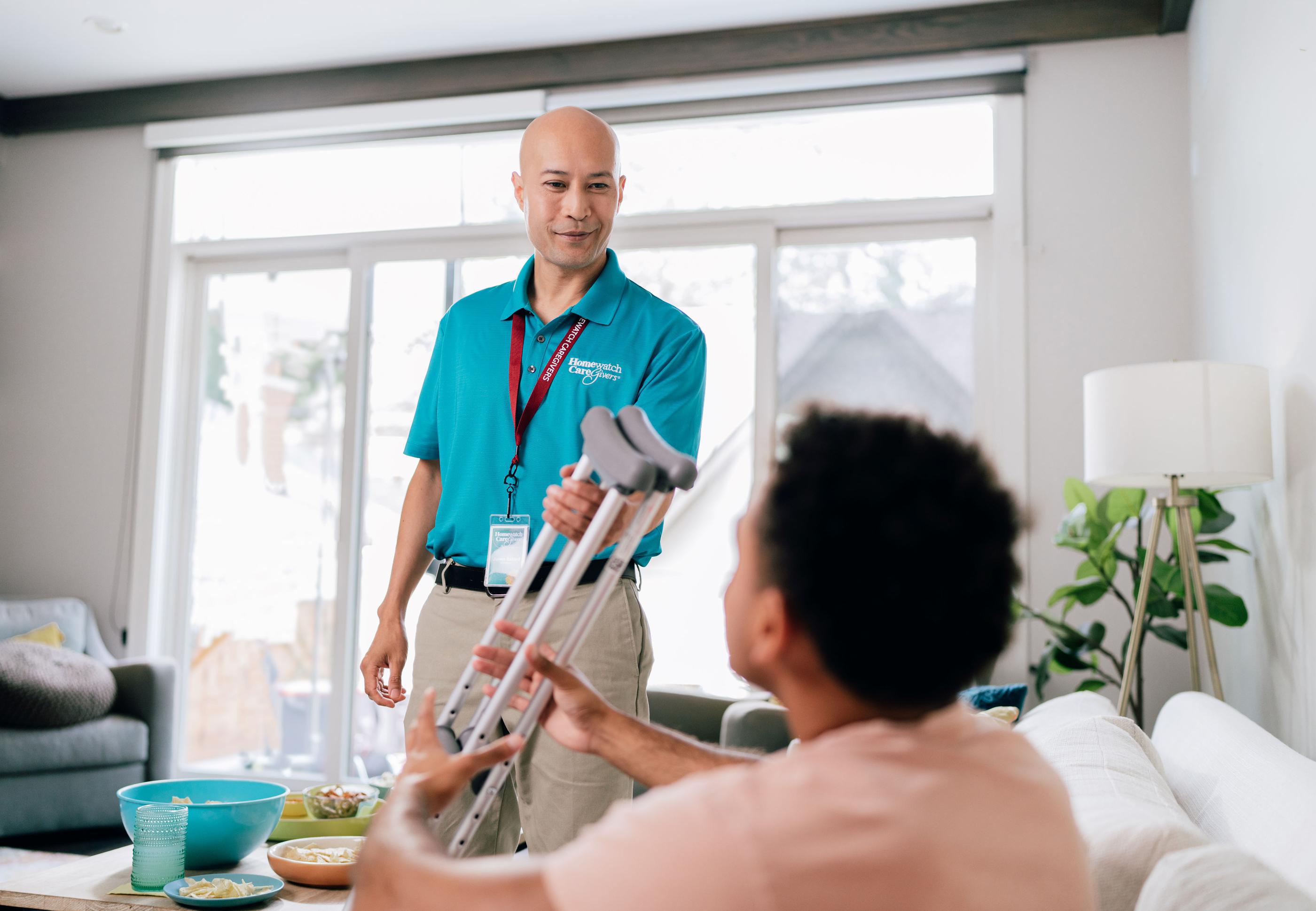 Caregiver handing crutches to woman on couch