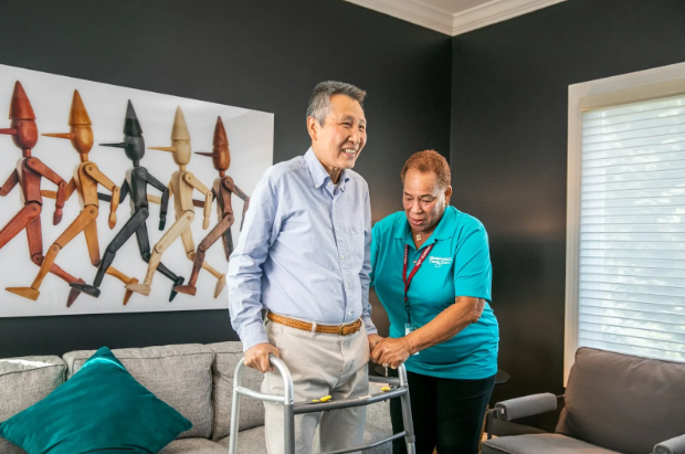 man standing and smiling with walker with woman helping him