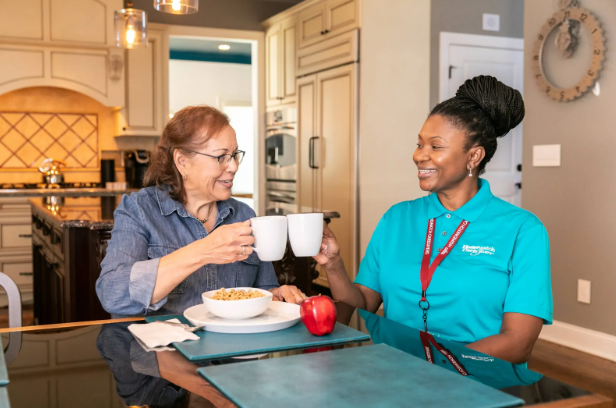 women clinking mugs and smiling at each other in kitchen